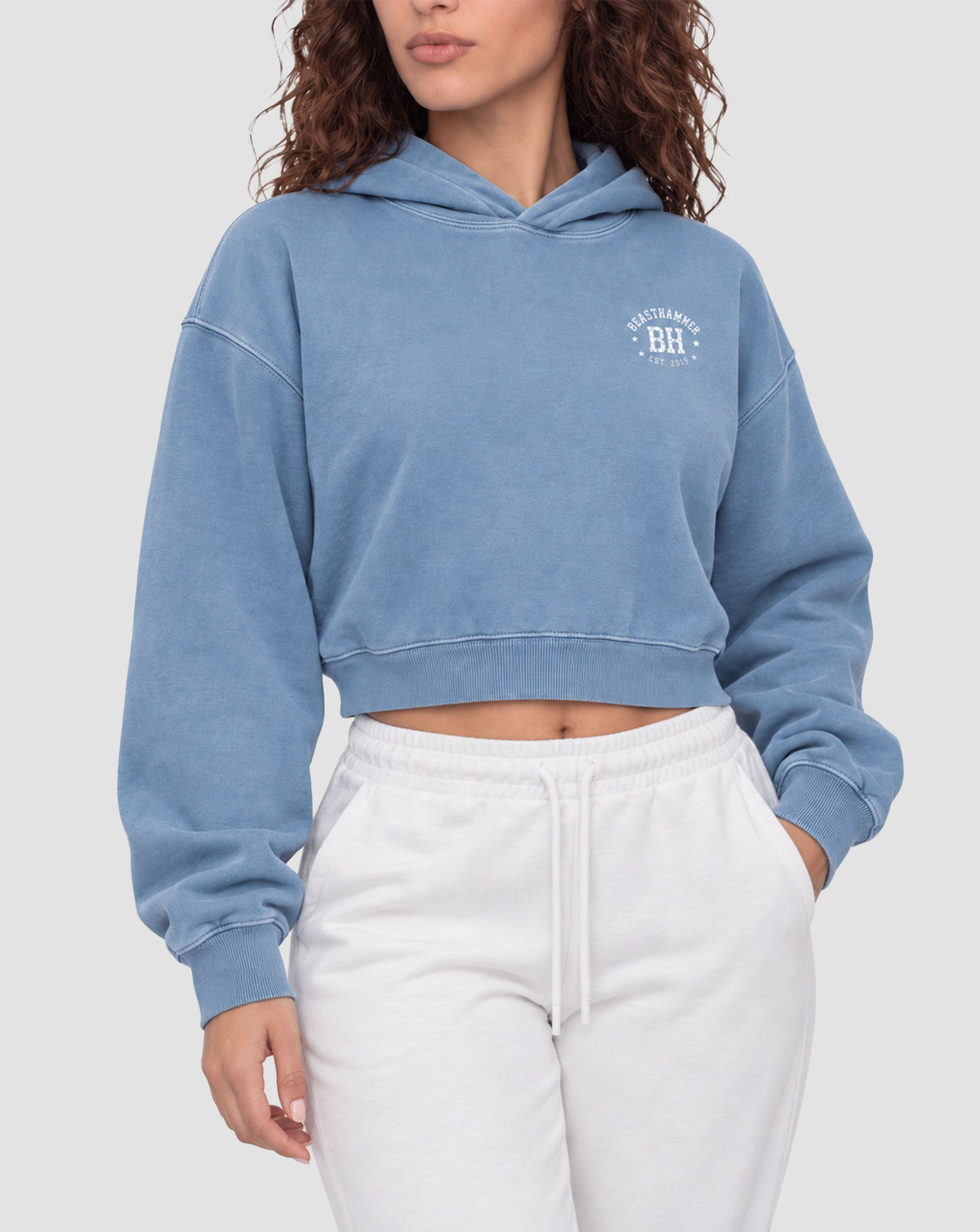 BEASTHAMMER Rest washed boxy hoodie in dusty blue, worn front view showing the boxy cropped fit and the BH badge on the chest