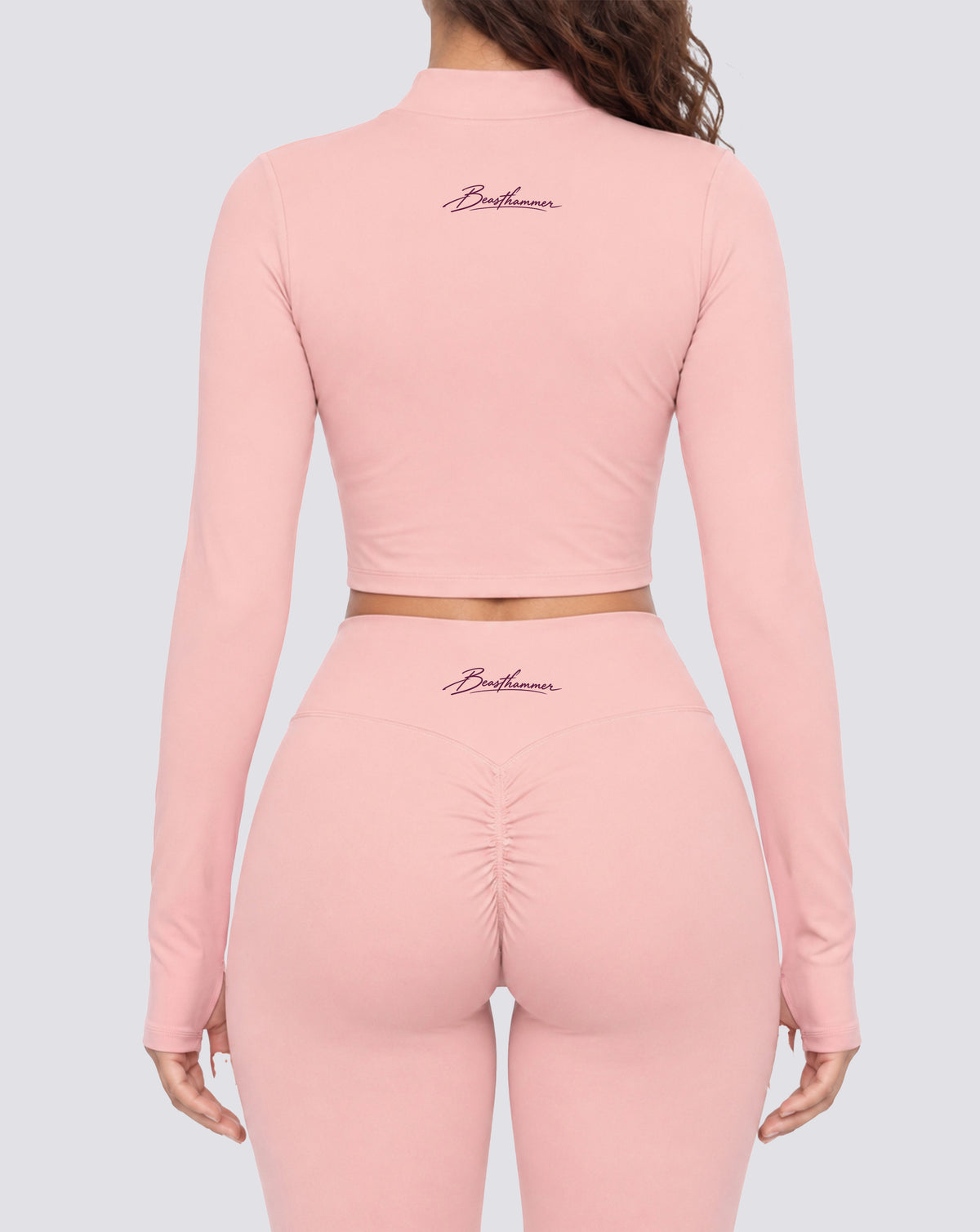 BEASTHAMMER Signature crop jacket in pink, worn back view with the handwritten Beasthammer script logo across the upper back, styled with matching Signature scrunch leggings