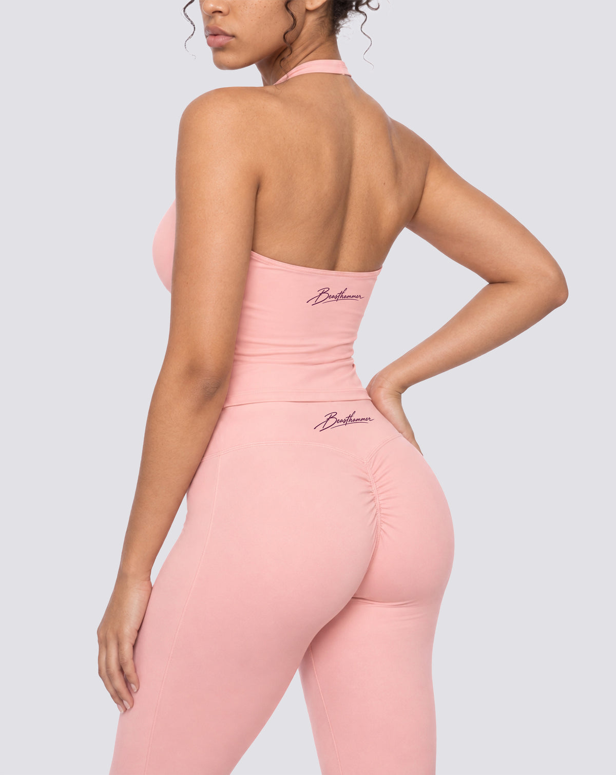 BEASTHAMMER Signature halter top in pink, worn back three-quarter view with the handwritten Beasthammer script logo, styled with matching Signature scrunch leggings