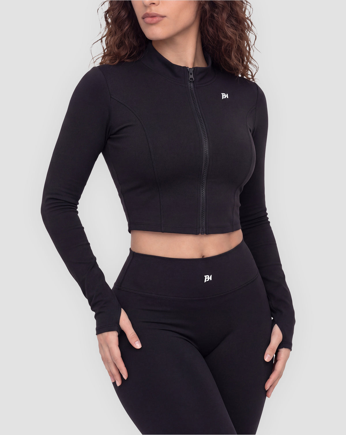 BEASTHAMMER Signature crop jacket in black, worn front view with stand collar, full zip and BH monogram, styled with matching Signature scrunch leggings
