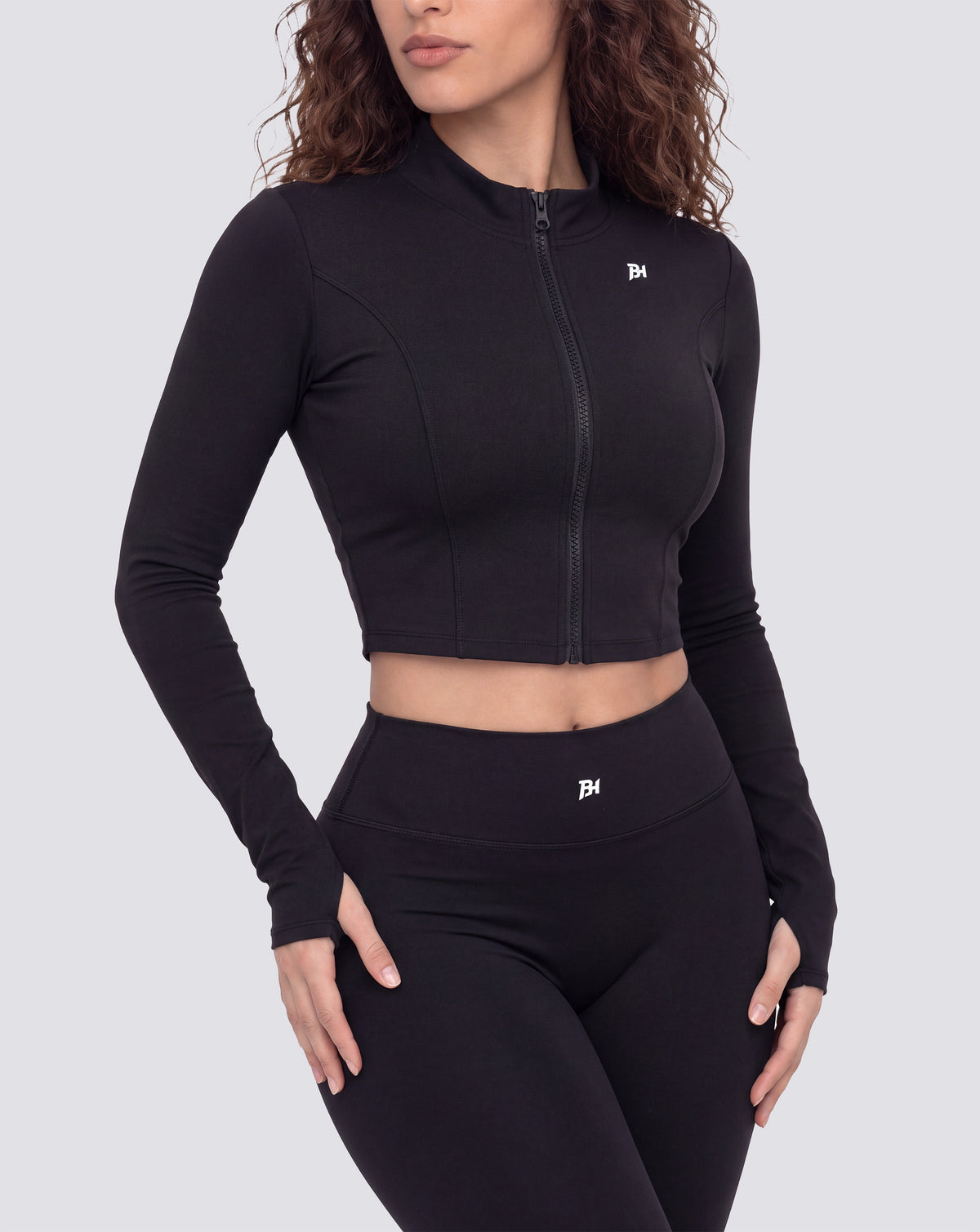 BEASTHAMMER Signature crop jacket in black, worn front view with stand collar, full zip and BH monogram, styled with matching Signature scrunch leggings