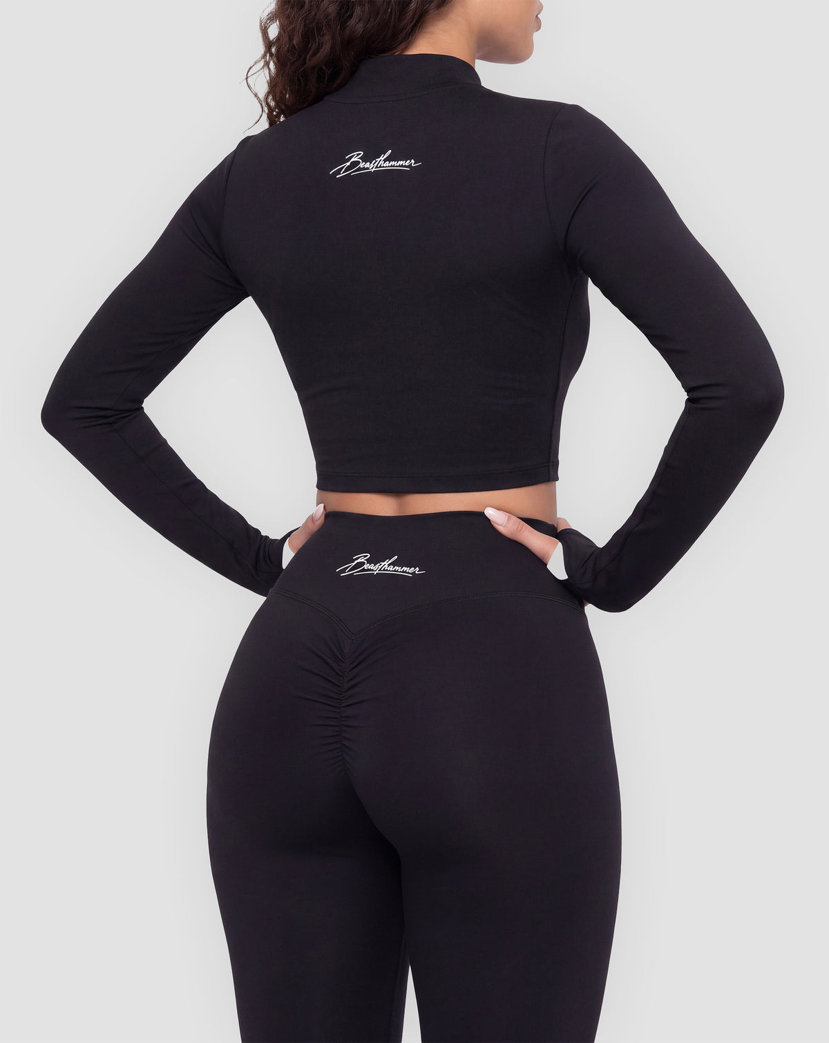 BEASTHAMMER Signature crop jacket in black, worn back view with the handwritten Beasthammer script logo across the upper back, styled with matching Signature scrunch leggings