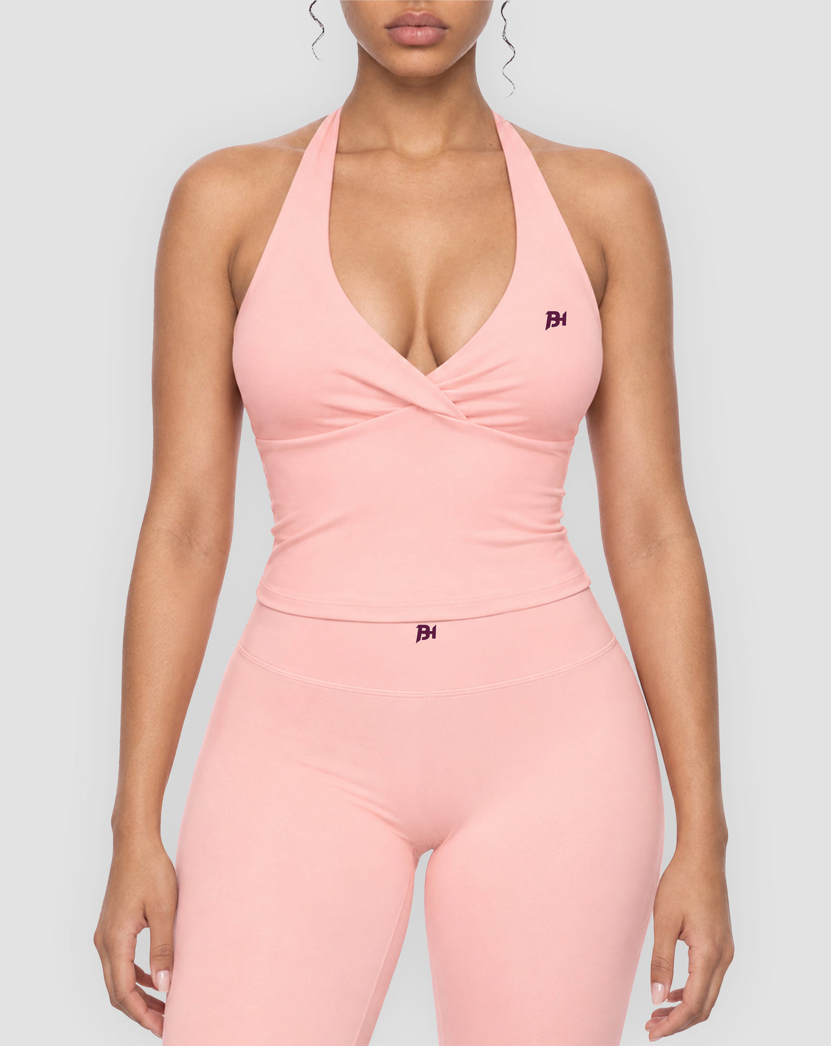 BEASTHAMMER Signature halter top in pink, worn front view with halter neck, ruched twist and BH monogram, styled with matching Signature scrunch leggings
