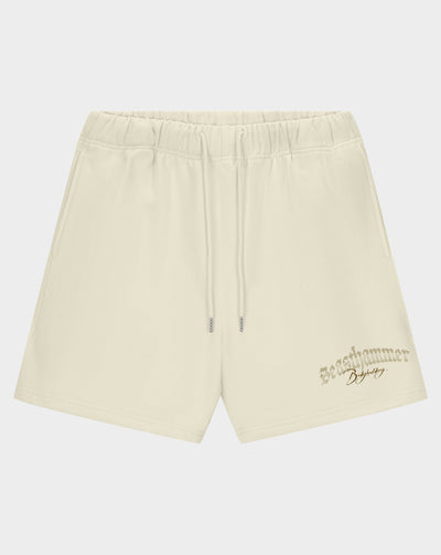 Cream-colored athletic shorts with an elastic drawstring waist and a small metallic logo on the lower left leg, displayed against a light gray background.