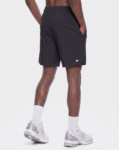 A person shown from the back wearing black athletic shorts, white socks, and white running shoes against a light gray studio background.