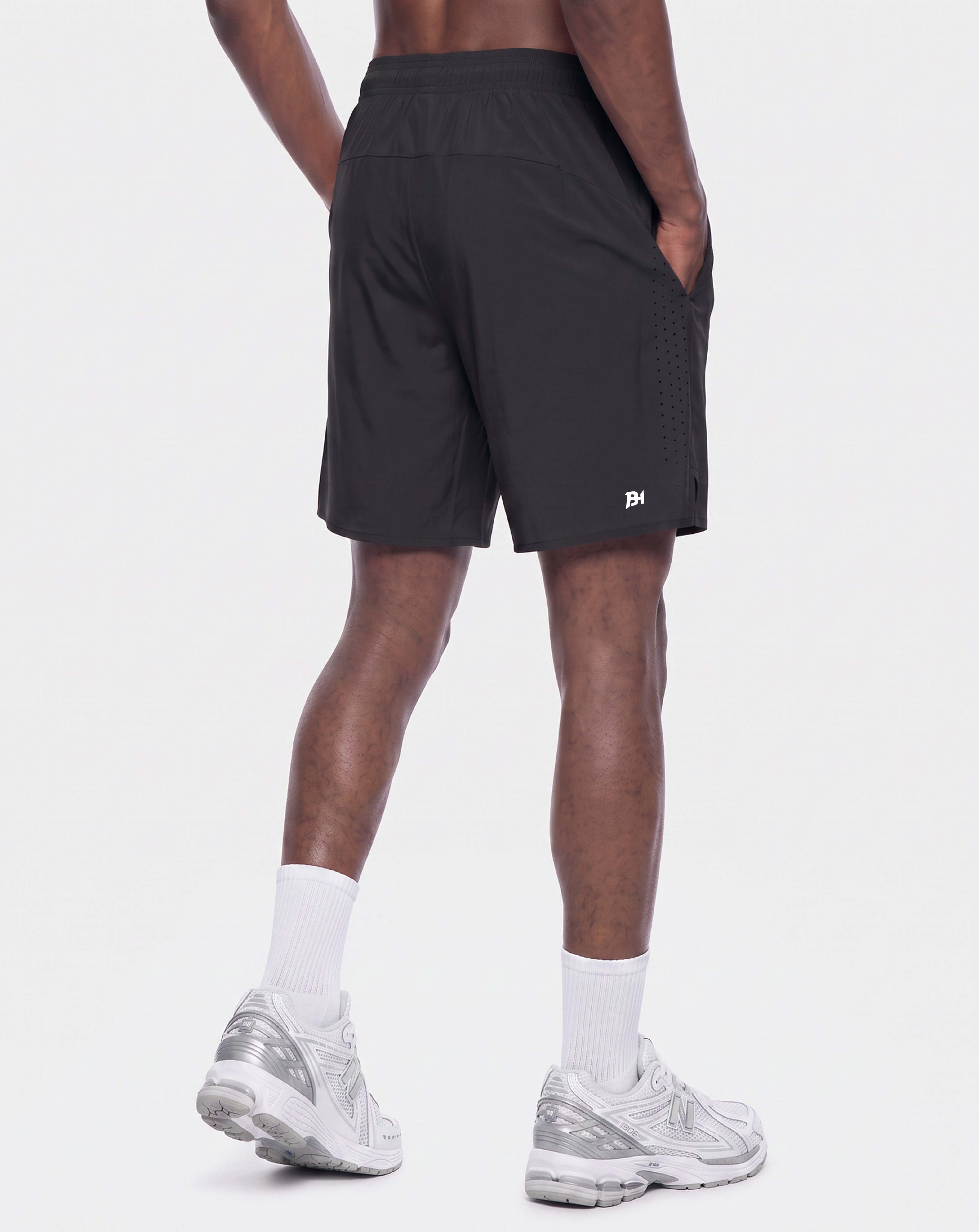 A person shown from the back wearing black athletic shorts, white socks, and white running shoes against a light gray studio background.